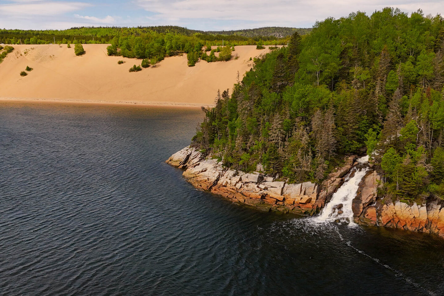 Vue aérienne des imposantes dunes de sable de Tadoussac et d'une chute d'eau se jetant directement dans le fleuve Saint-Laurent.