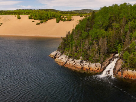 Vue aérienne des imposantes dunes de sable de Tadoussac et d'une chute d'eau se jetant directement dans le fleuve Saint-Laurent.