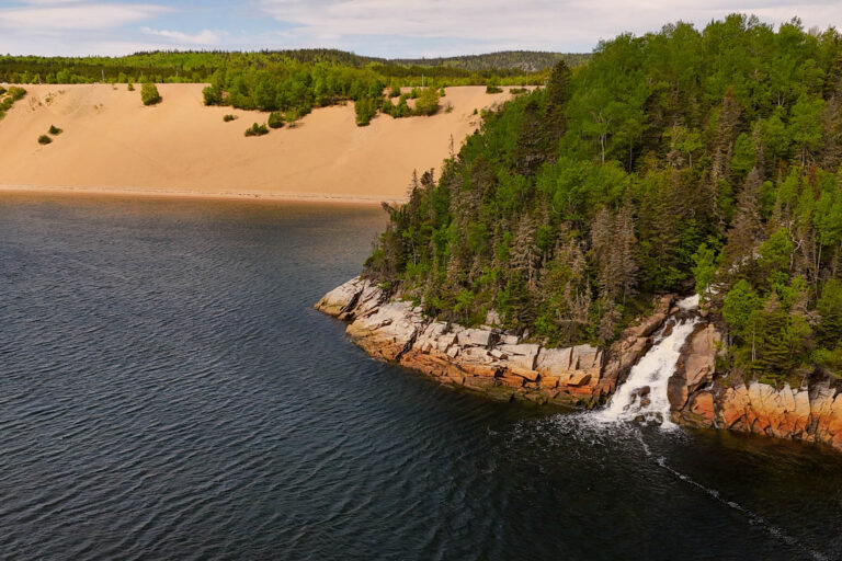 Vue aérienne des imposantes dunes de sable de Tadoussac et d'une chute d'eau se jetant directement dans le fleuve Saint-Laurent.