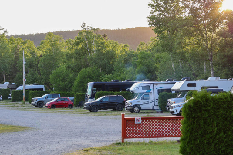 Plusieurs VR et caravanes motorisées stationnés dans un camping boisé à Tadoussac, Québec, au coucher du soleil.