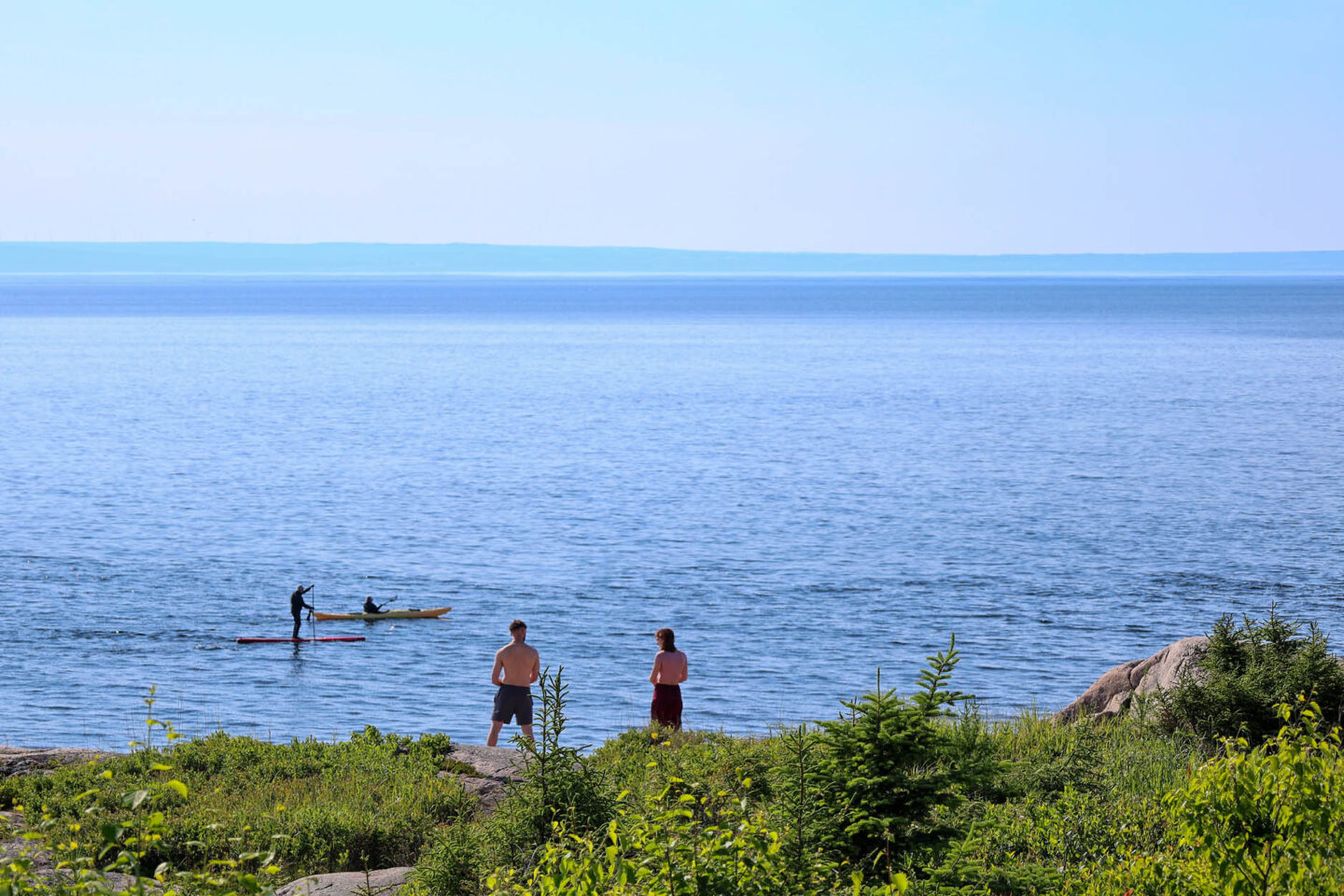 Personnes pratiquant le kayak de mer et la planche à pagaie (paddleboard) sur les eaux calmes du fleuve Saint-Laurent près du rivage.
